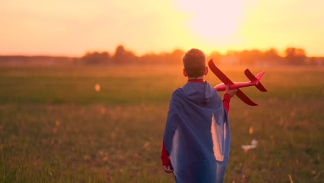 Boy-in-runs-in-a-red-raincoat-holding-a-plane-laughing-at-sunset-in-the-summer-field-imagining-that-he-is-an-airplane-pilot-playing-with-a-model-airplane
